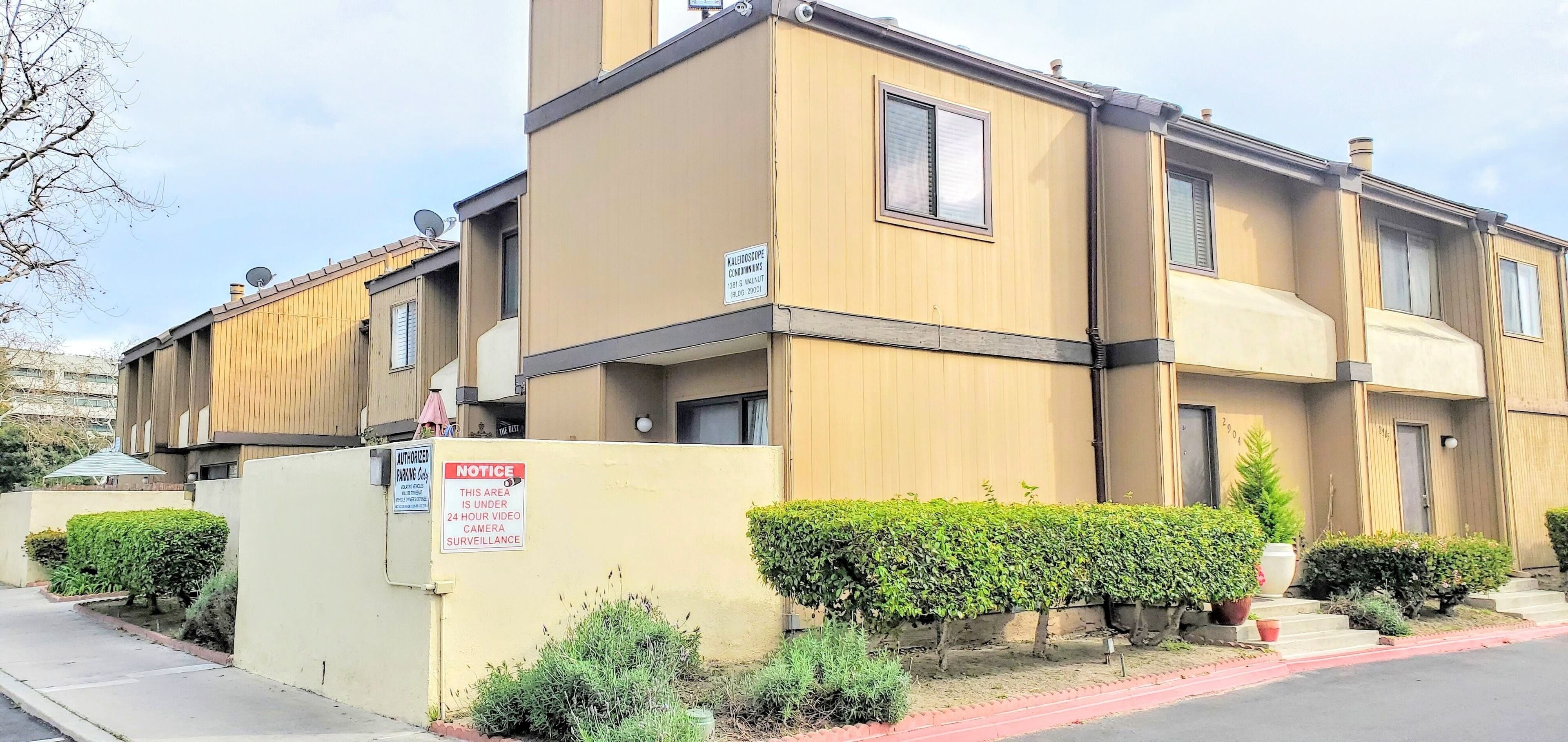 Edificio residencial de varios pisos con fachada color beige, antena parabólica y un cartel que indica vigilancia por video las 24 horas.