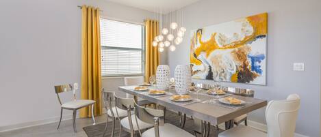 A dining room with a long table, six chairs, and a large abstract painting on the wall.