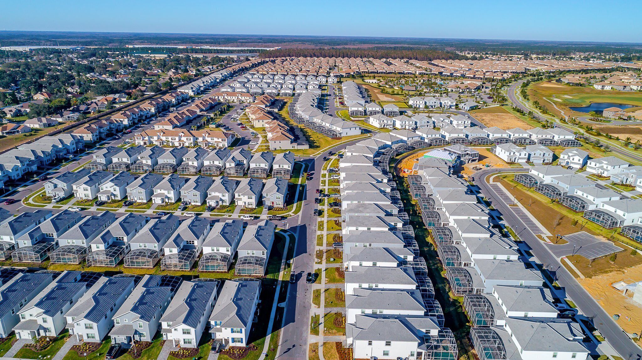 A residential area with multiple rows of houses, roads, and a golf course in the background.
