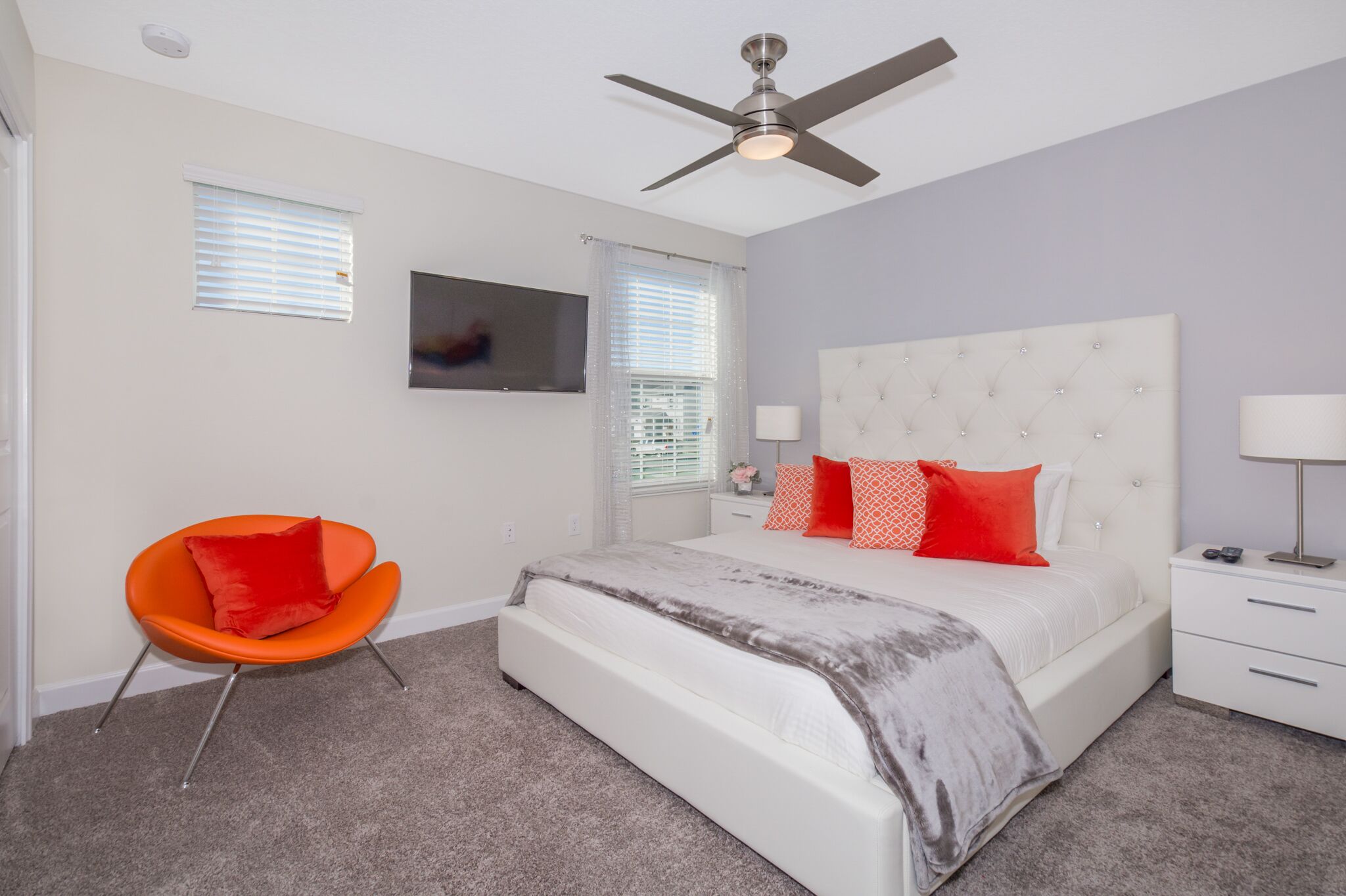 A bedroom with a bed, a chair, a ceiling fan, and a TV on the wall.
