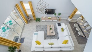 Ein modernes Wohnzimmer mit einem Ecksofa, einem Couchtisch und einem Fernseher. Es gibt einen Essbereich mit Tisch und Stühlen.