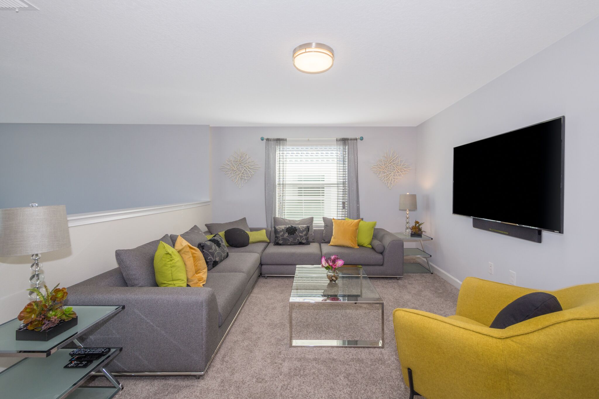 A living room with a grey sofa, yellow armchair, and a flat-screen TV mounted on the wall.