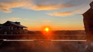 Een zonsondergang boven een kustgebied, met een gebouw links en een grote rotsformatie rechts.