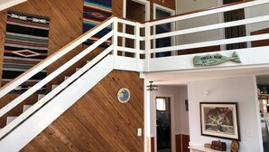 Een houten interieur met een trap, een wandklok, een lijst met een afbeelding en een bord waarop 'STELLA BLUE' staat.