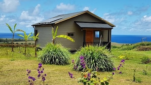 A small, single-story house with a sloped roof, solar panels, and a view of the ocean. - Maunga roa eco lodge (Hanga Roa)