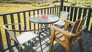 Une terrasse dotée d’une table ronde en verre et de deux chaises en osier, offrant une vue sur un paysage verdoyant.