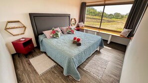 A bedroom with a large bed, a nightstand, a window with a view of the countryside, and a wooden floor.