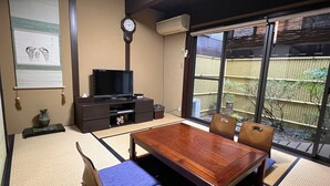 A traditional Japanese room with tatami flooring, a low wooden table, a television, and a sliding door to a garden. - Maeniiya Machiya Inn (Kyoto)