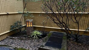 A garden with a bamboo fence, a stone lantern, and various plants. - Maeniiya Machiya Inn (Kyoto)