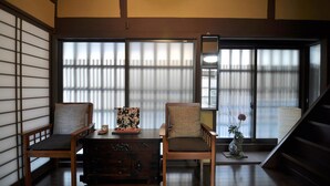 A traditional Japanese room with tatami flooring, a low wooden table, two chairs, a decorative vase, and a sliding door with shoji screens. - Maeniiya Machiya Inn (Kyoto)