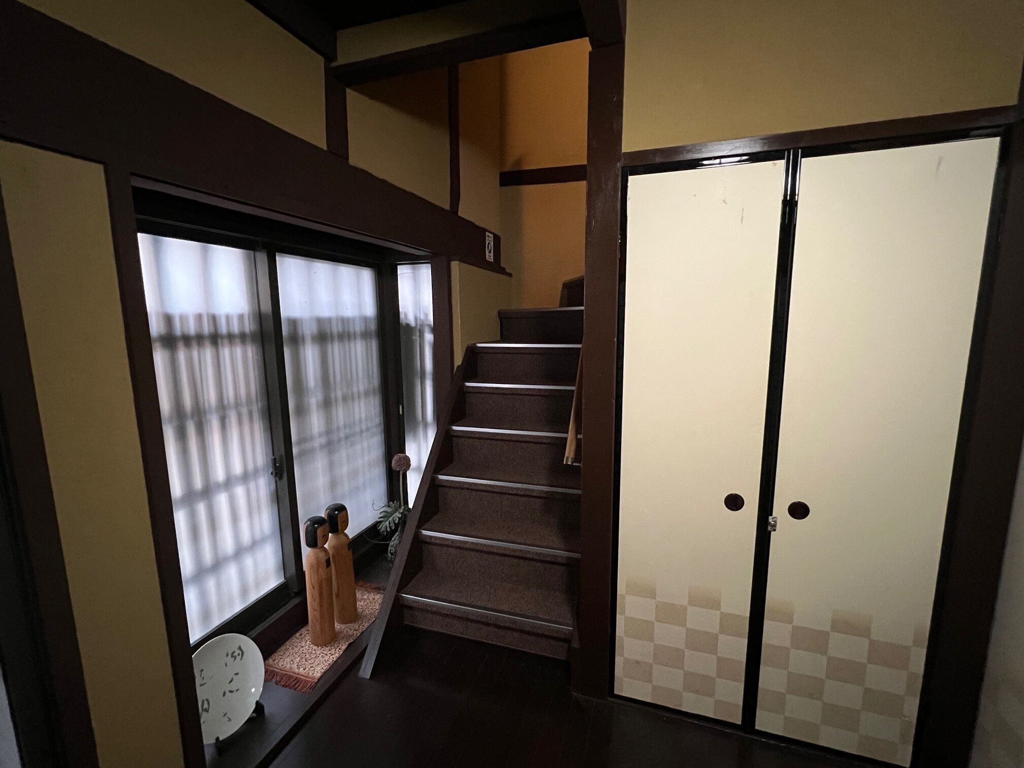 A traditional Japanese interior with a wooden staircase, sliding doors, and a window with a view.