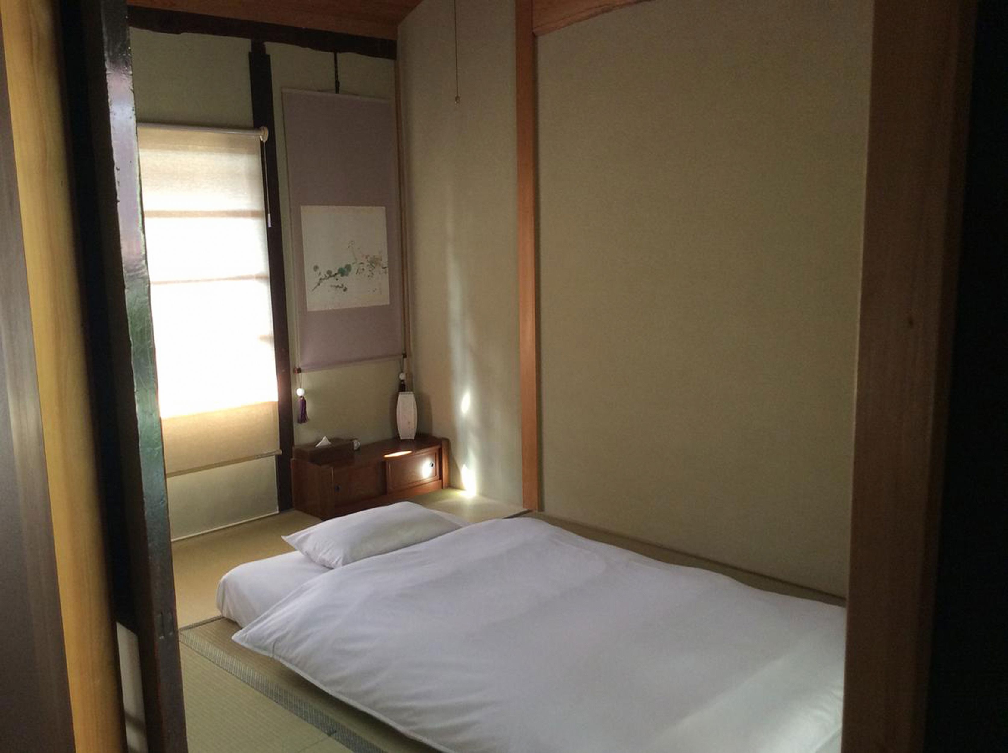 A room with a bed, a small wooden nightstand, a wall-mounted shelf, and a framed picture.