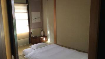 A room with a bed, a small wooden nightstand, a wall-mounted shelf, and a framed picture.