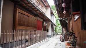 A narrow alleyway with traditional wooden buildings, a metal fence, and potted plants. - Kiyomizu Machiya Inn (Kyoto)