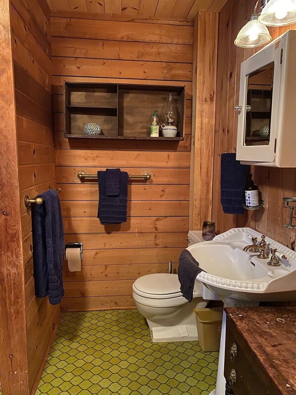 A compact wooden bathroom with a toilet, sink, and a shelf above the toilet.