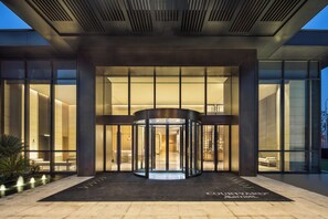 A modern hotel entrance with a revolving door, large glass windows, and a well-lit interior.