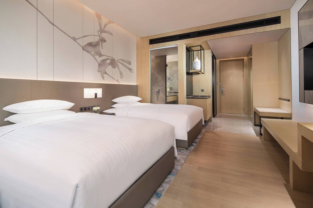 Ein Hotelzimmer mit zwei Betten, einer Sitzecke, einem Fernseher und einem durch eine offene Tür einsehbaren Badezimmer.