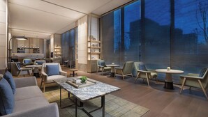 Een moderne hotel lobby met een zithoek, een bar en een groot raam met uitzicht op de omgeving.