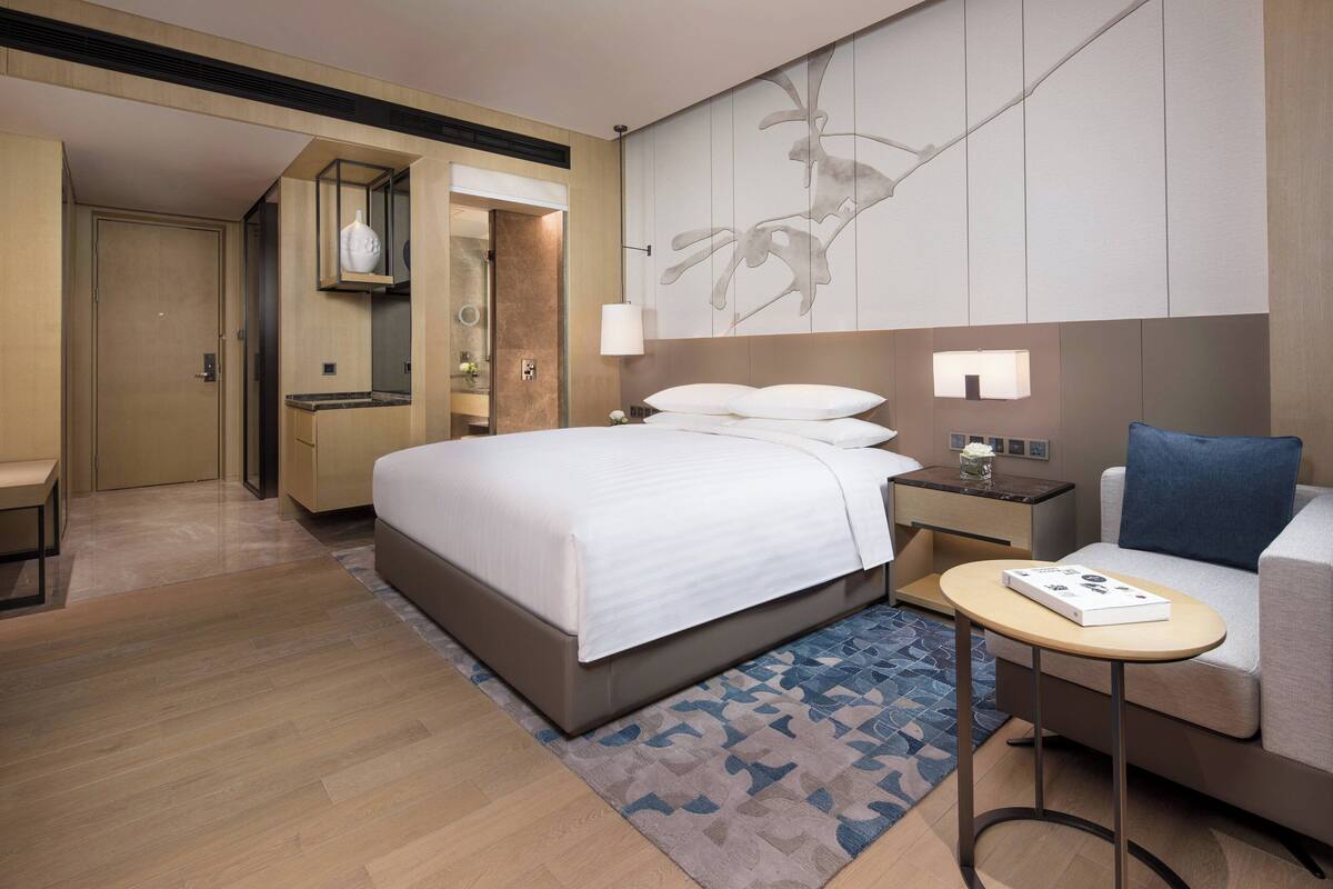 Ein modernes Hotelzimmer mit einem großen Bett, einem kleinen Tisch, einer Couch und einem durchgegangenen Tür erkennbaren Badezimmer.