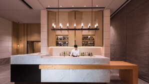 Een moderne bar met een marmeren aanrecht, een houten bank en een barman.