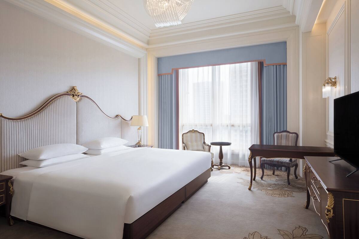 Une chambre d’hôtel avec un grand lit, un bureau, une chaise, une télévision et une fenêtre avec des rideaux.