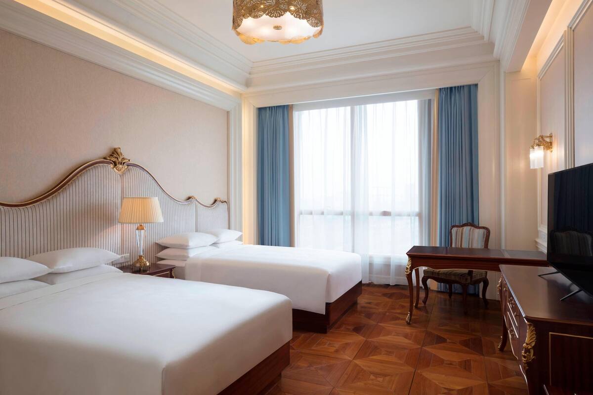 Une chambre d’hôtel avec deux lits, un bureau, une télévision et une grande fenêtre avec des rideaux.