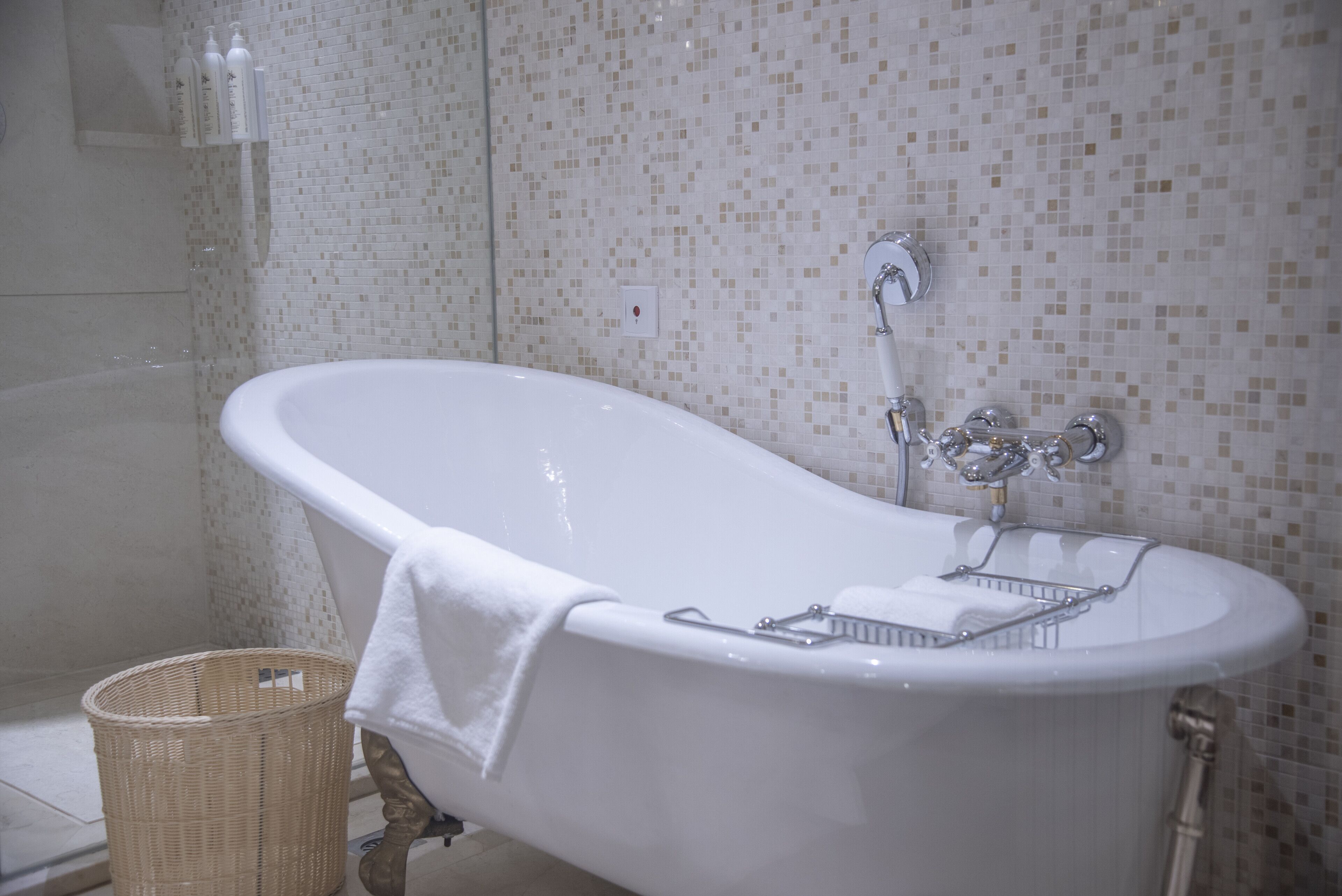Une salle de bain avec une baignoire sur pieds, un panier en osier et un mur carrelé.