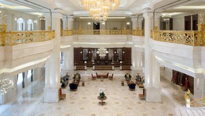 Un vaste hall d’entrée avec un plafond haut, de magnifiques lustres et un espace central aménagé avec de nombreux fauteuils et tables.
