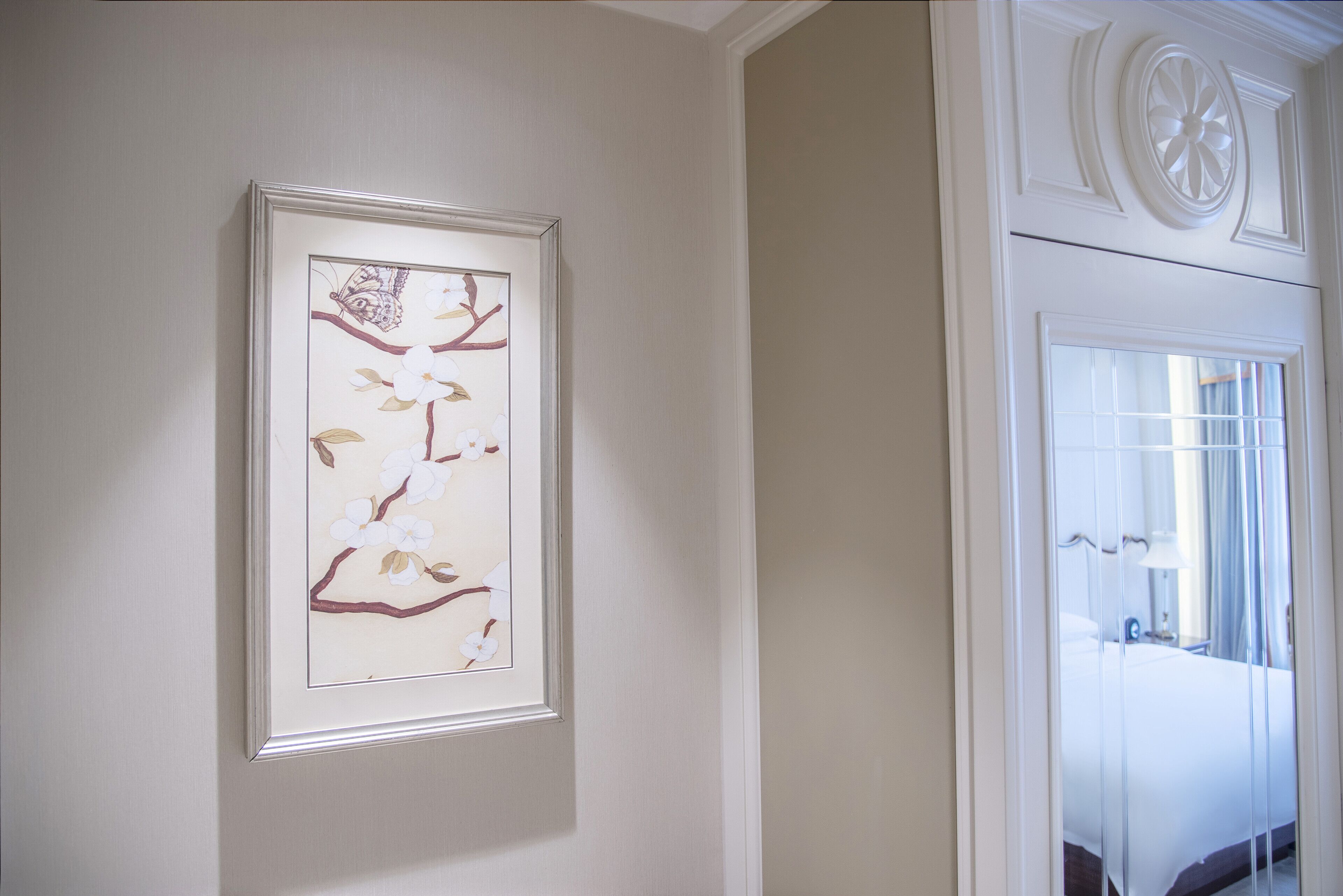 A framed artwork of a branch with flowers and a butterfly on a wall.