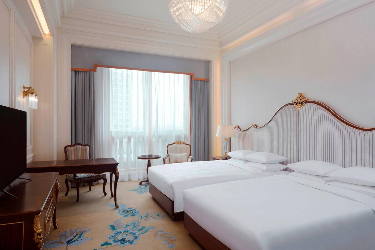 Une chambre d’hôtel avec deux lits, un bureau, une télévision et un lustre.