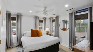 A hotel room with a large bed, a ceiling fan, and a view of the outside. - Charming Historic 1BR w/ Private Porch + Free Parking (Charleston)