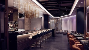 A modern bar area with a long counter, multiple bar stools, and a unique hanging light fixture.