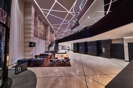 A spacious lobby with a modern design, featuring a seating area with sofas and armchairs, a staircase, and a 'Hilton' sign.