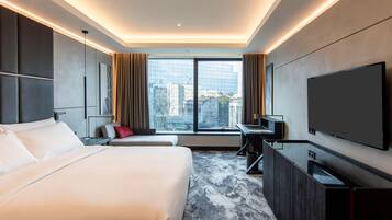 Habitación de hotel moderna con una cama grande, un escritorio, un televisor y vistas a la ciudad.