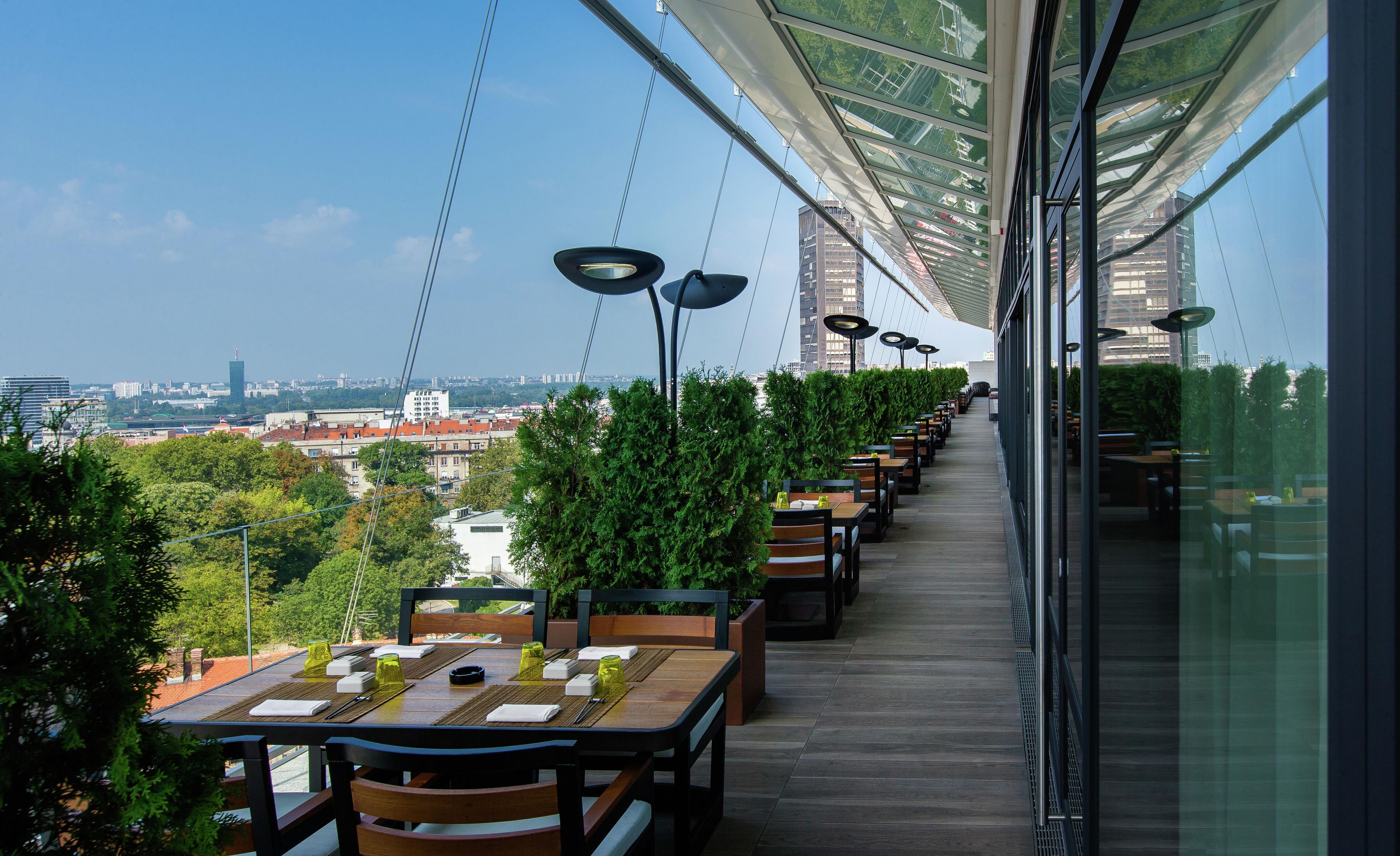 Un restaurante en la azotea con mesas al aire libre, vistas a la ciudad y arquitectura moderna.
