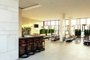 A spacious indoor area with a bar, seating, and large windows. - Hilton Belgrade (Belgrade)