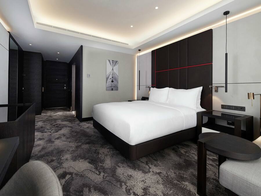 Une chambre d’hôtel moderne avec un grand lit, un bureau, une chaise, une télévision et un coussin décoratif rouge.