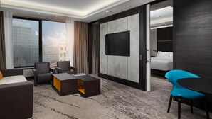 A hotel room with a large window, a flat-screen TV, a bed, a coffee table, and seating.
