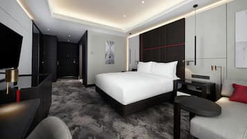 A modern hotel room with a large bed, a desk, a chair, a TV, and a red accent pillow.