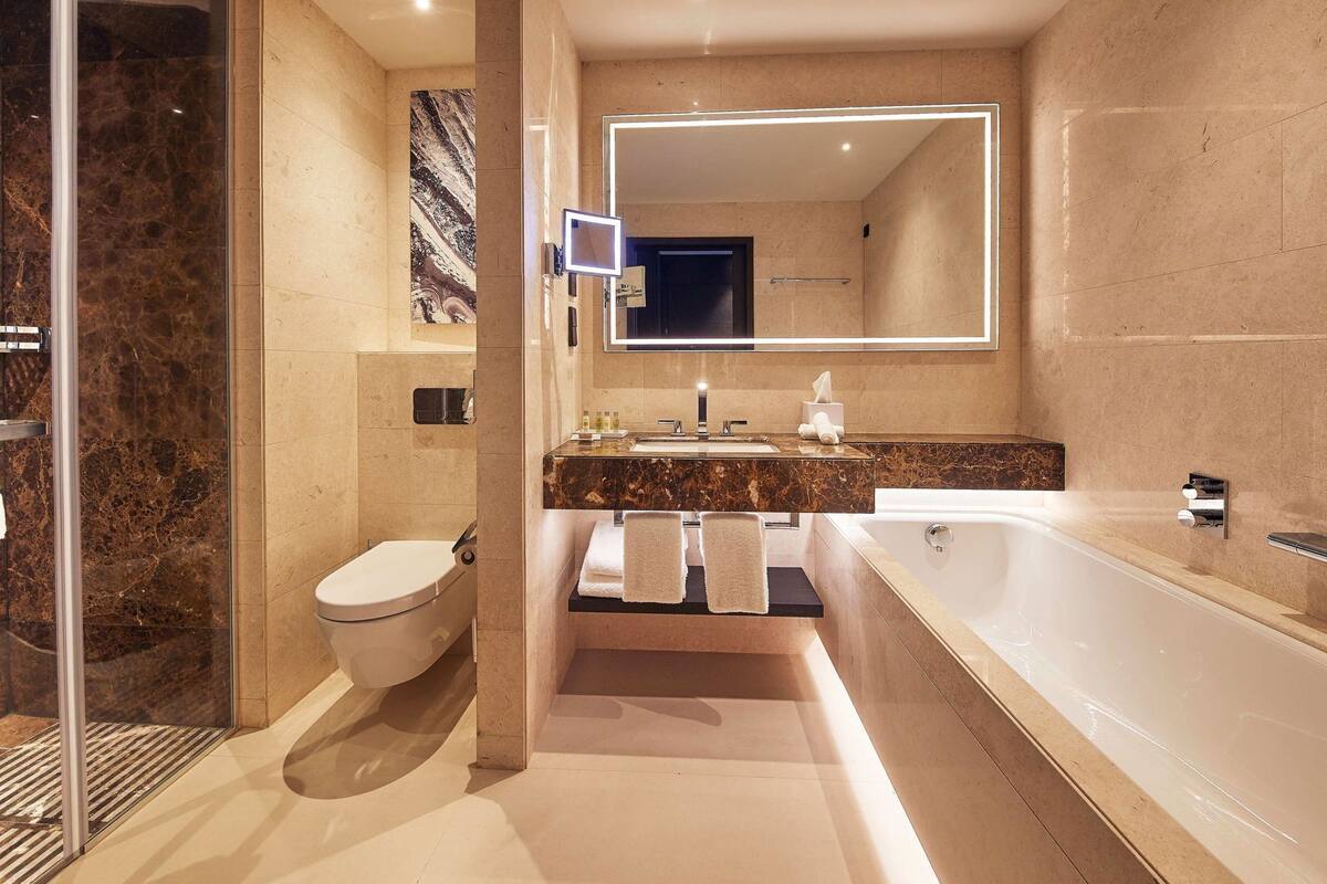 Un baño moderno con cabina de ducha de vidrio, inodoro, lavamanos con encimera de mármol, espejo grande y bañera.