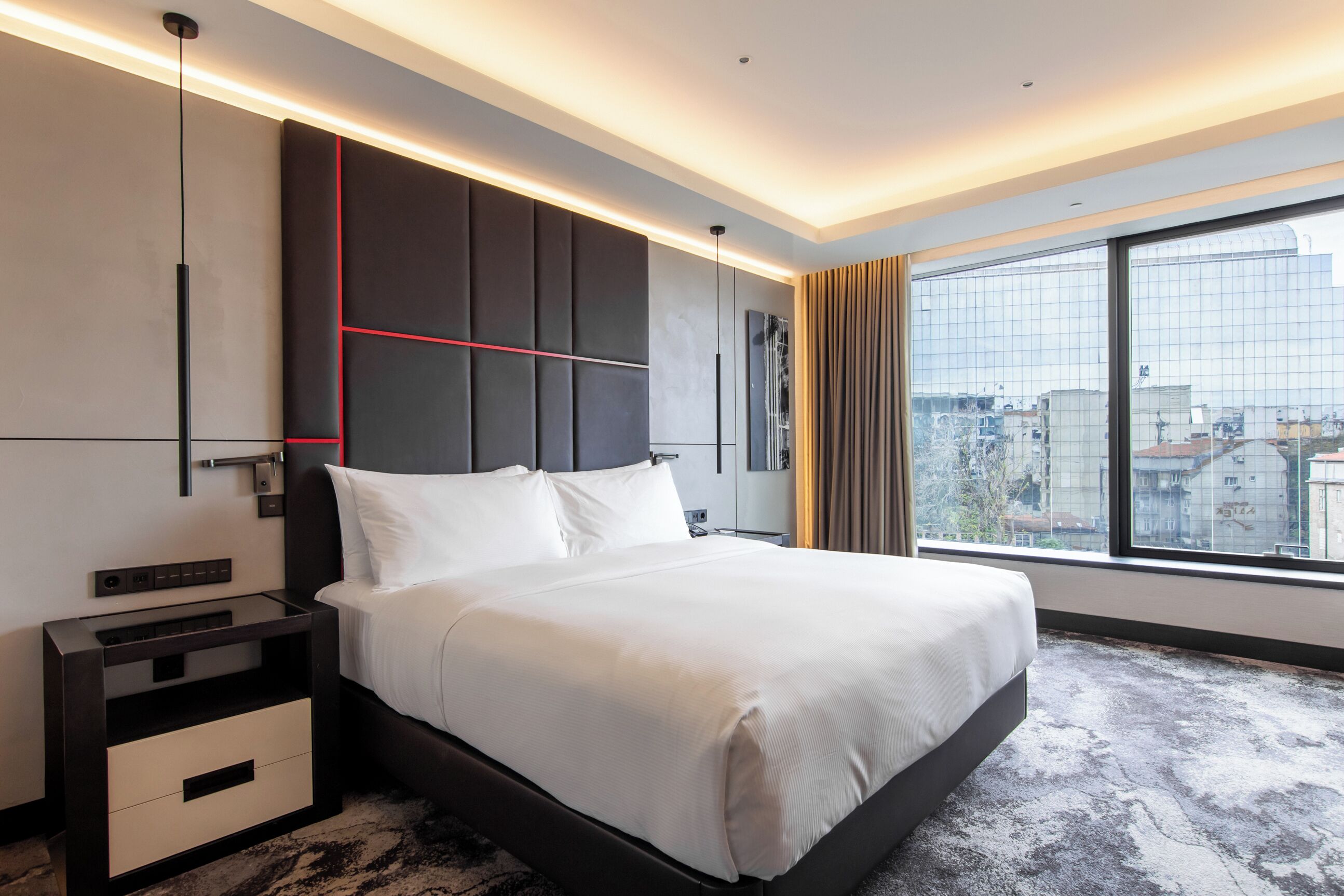 Een moderne hotelkamer met een groot bed, een nachtkastje, een aan de muur bevestigde televisie en een groot raam met uitzicht op de stad.