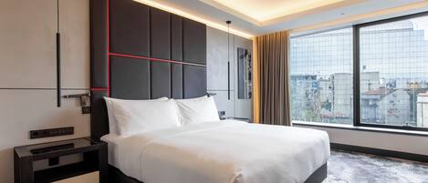 Een moderne hotelkamer met een groot bed, een nachtkastje, een aan de muur bevestigde televisie en een groot raam met uitzicht op de stad.