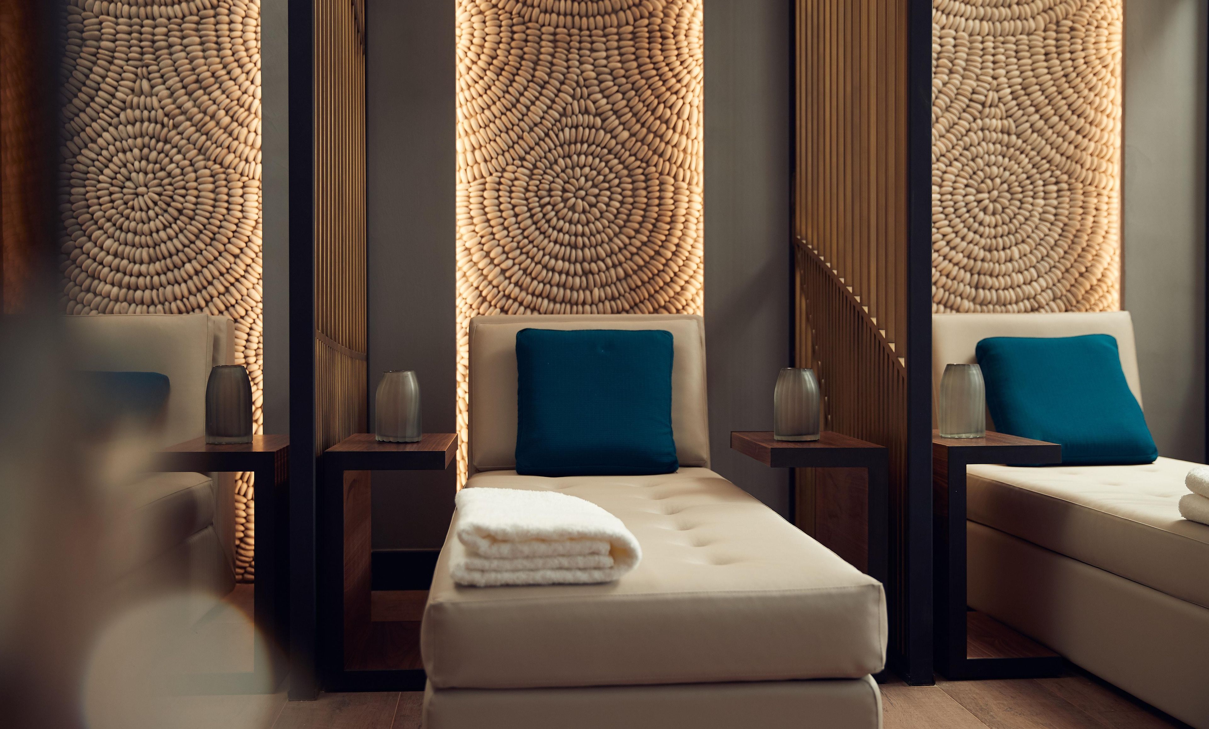 Un spa moderno con una camilla de masaje, dos mesitas auxiliares y paneles decorativos en la pared.