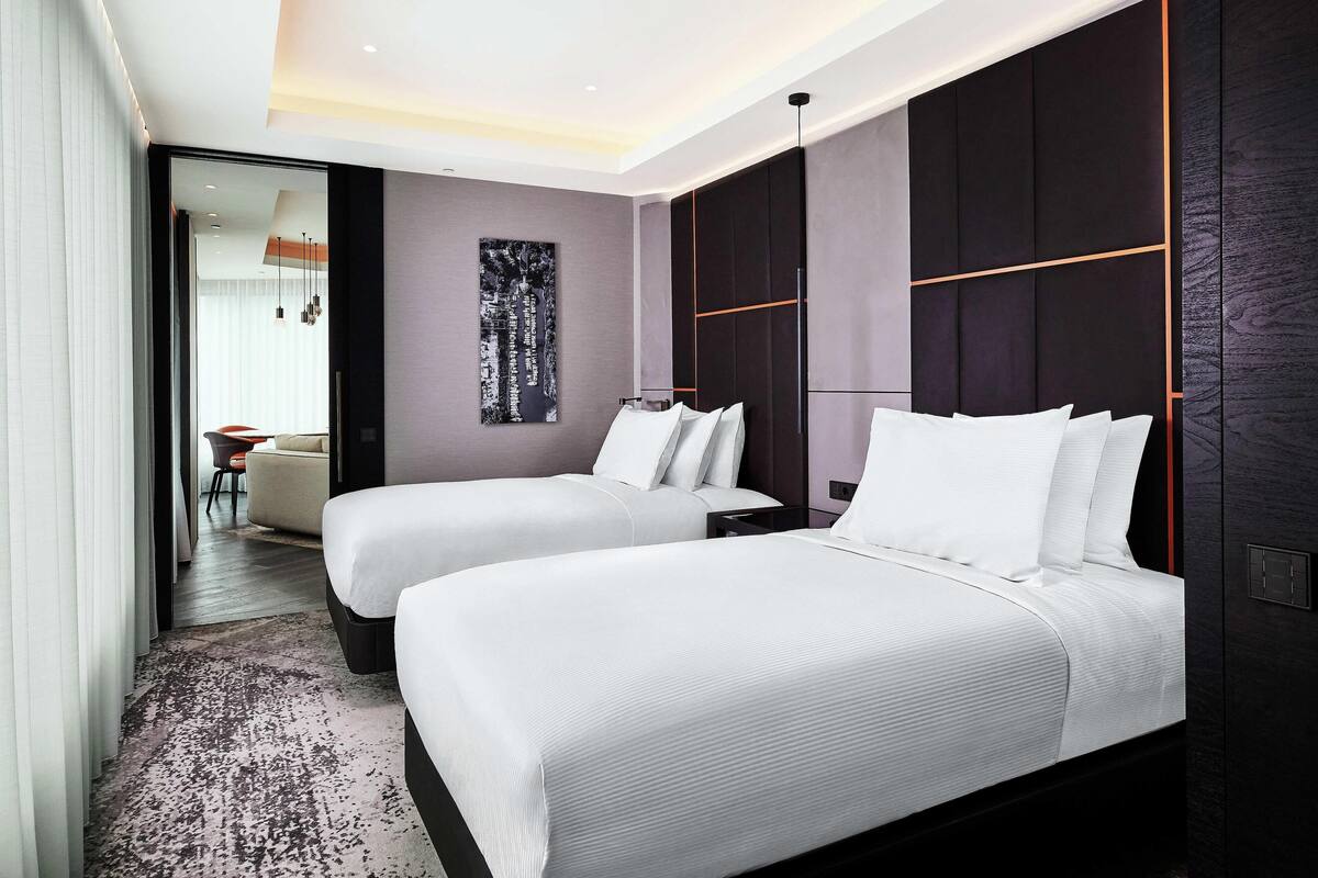 Habitación de hotel moderna con dos camas, una obra de arte abstracta grande en la pared y vistas a otra habitación.