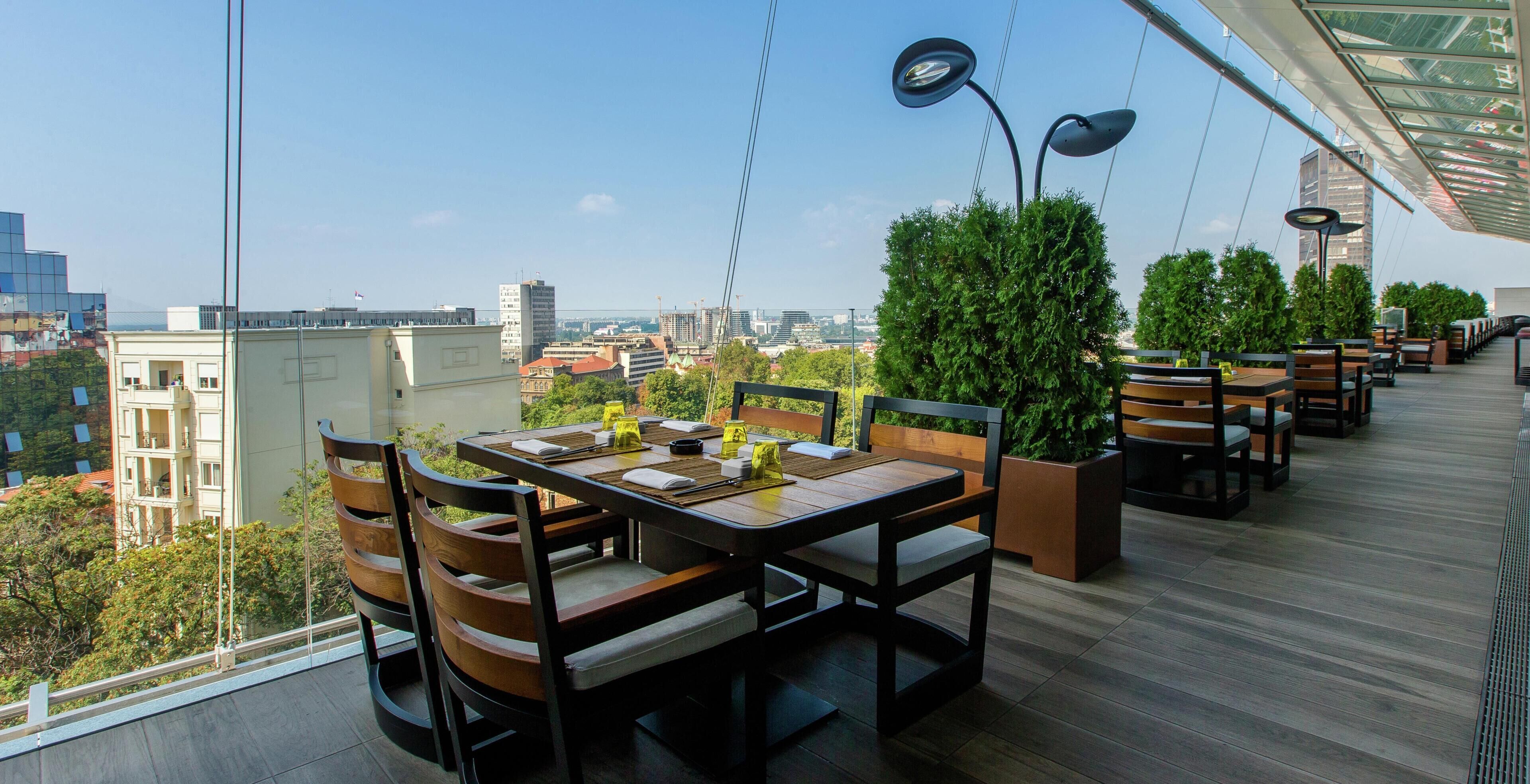 A rooftop dining area with tables, chairs, and potted plants.