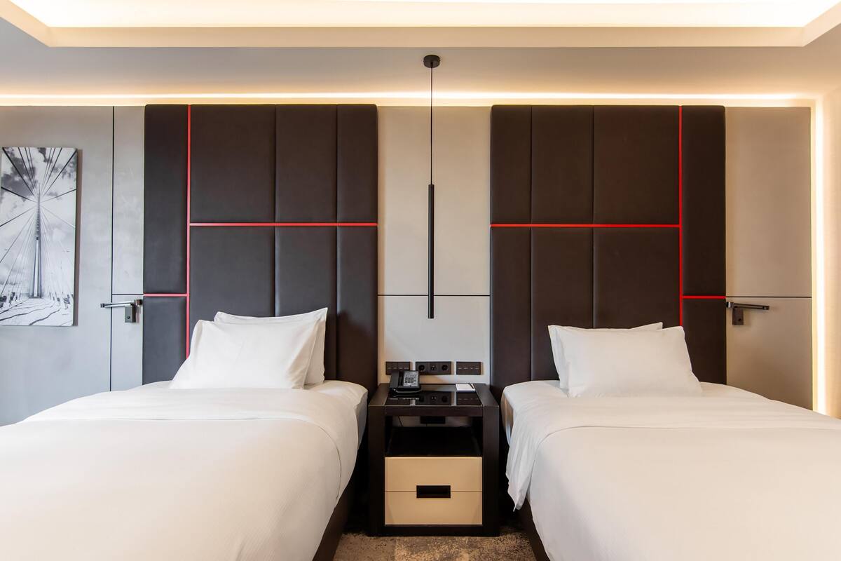 Una habitación de hotel moderna con dos camas, una mesita de noche con teléfono y un panel de control en la pared.