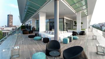 A rooftop terrace with seating, a glass-enclosed area, and a view of the city.
