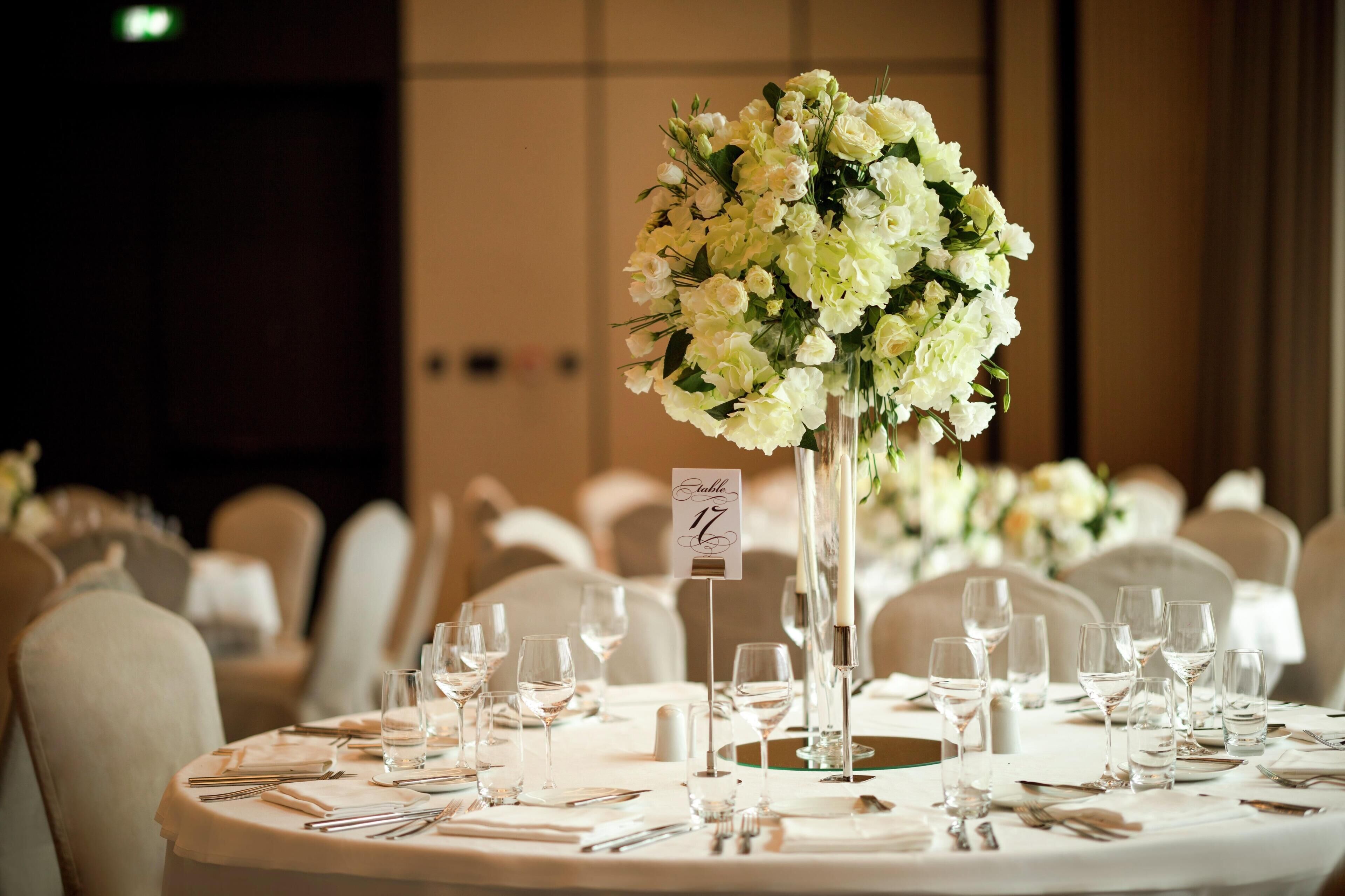Une table de banquet agrémentée d’un centre de table floral, de marque-places numérotés et de couverts disposés.