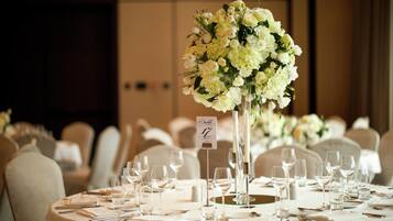 Une table de banquet agrémentée d’un centre de table floral, de marque-places numérotés et de couverts disposés.