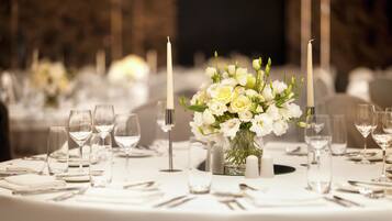 A round table with a white tablecloth, a vase of white flowers, candles, and empty wine glasses.